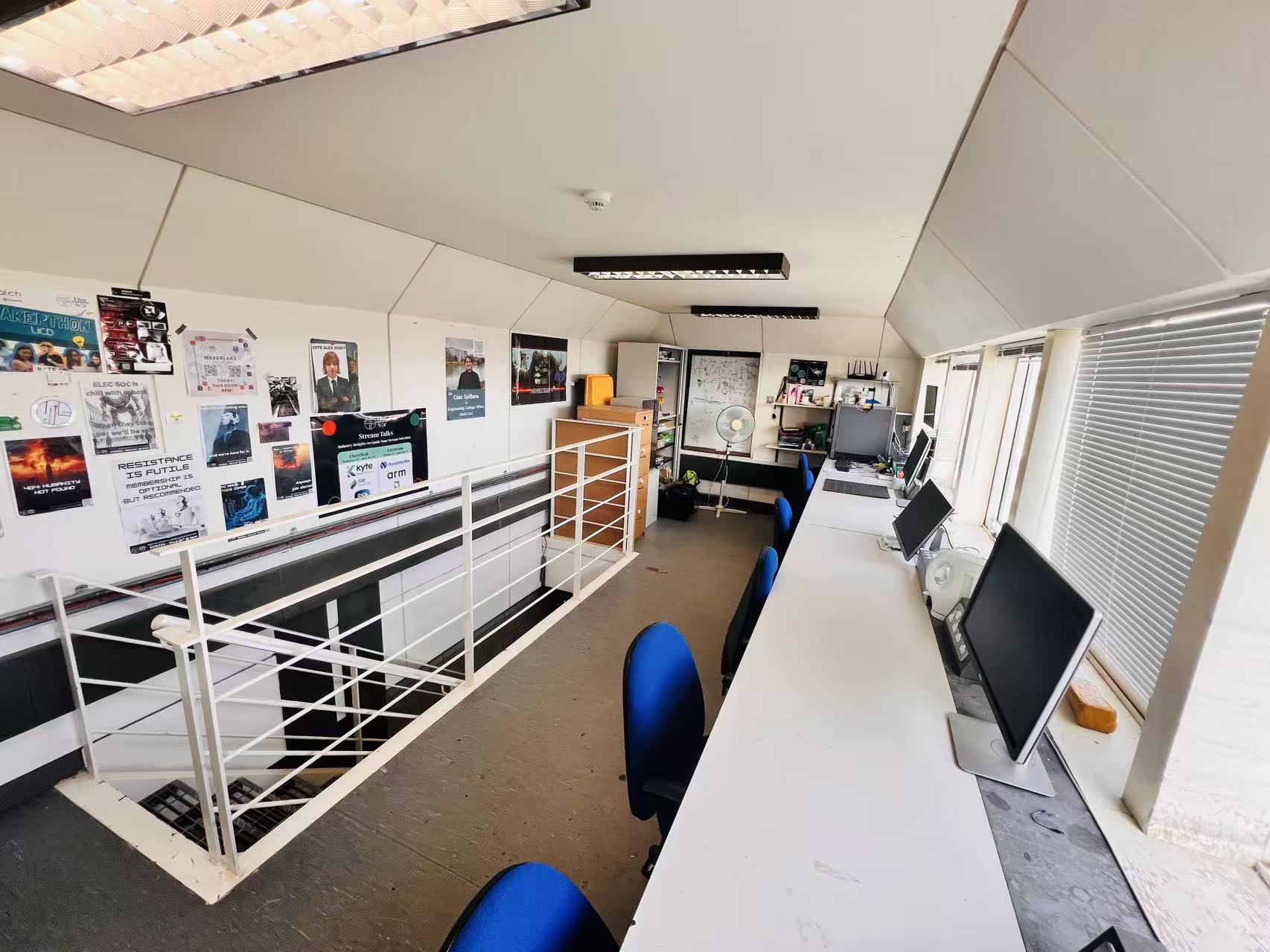Interior of the ElecSoc Lair: workbenches with monitors along the windows and posters on the wall